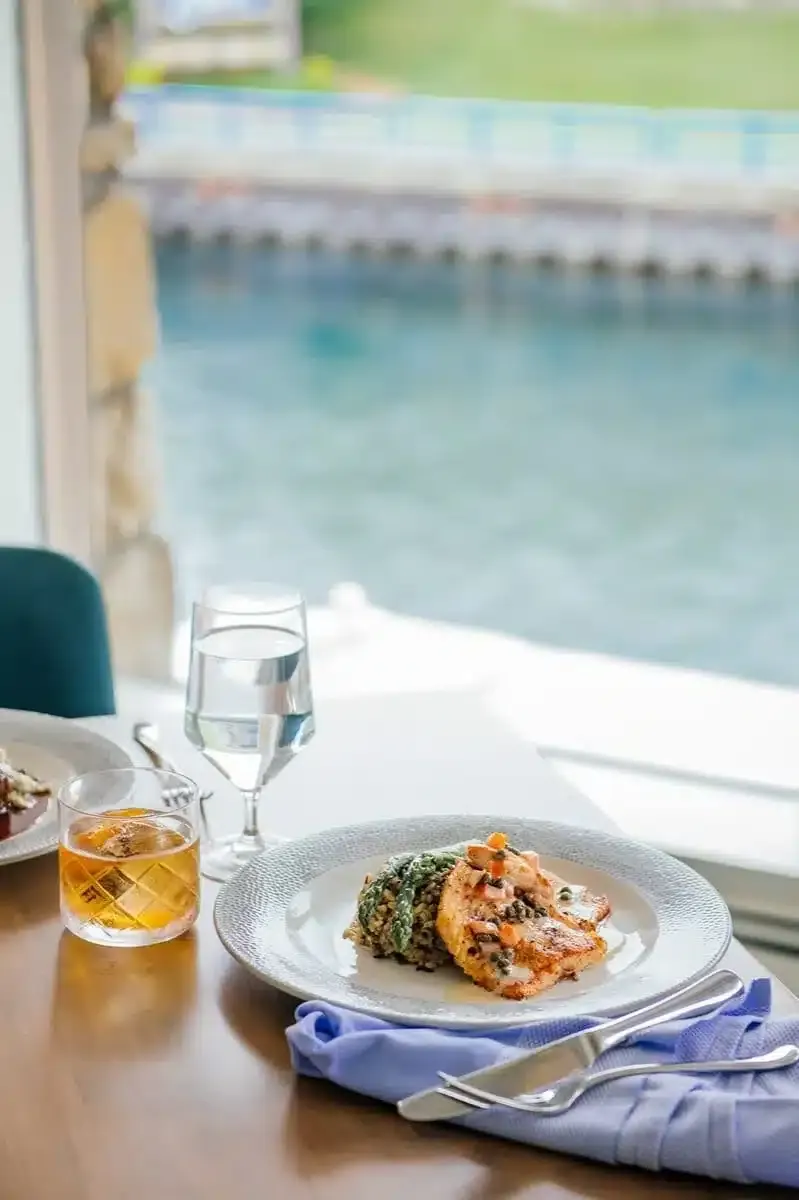 A seared fish plate on a table beside a sunlit window
